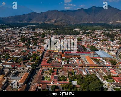 Beautiful aerial cinematic footage of the Antigua City in Guatemala, Its yellow church, the Santa Catalina Arch and the Acatenango Volcano Stock Photo