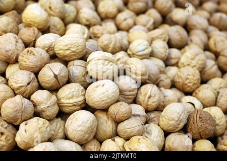 Walnuts heap for background. Dry nuts in shells on a market, protein food for brain health Stock Photo