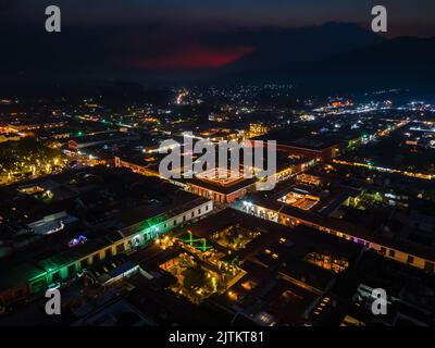 Beautiful aerial cinematic footage of the Antigua City in Guatemala, Its yellow church, the Santa Catalina Arch and the Acatenango Volcano Stock Photo