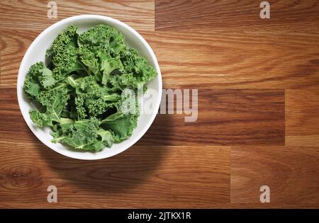 Chopped kale in white bowl shot from above on wooden table, with space to add copy Stock Photo