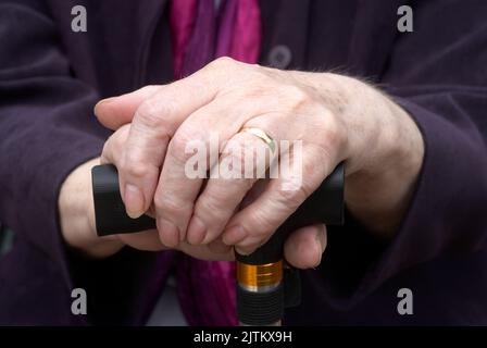 Close up of elderly womans hands resting on her walking stick Stock Photo