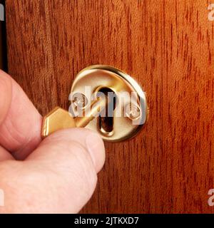 Close up of male hand using a brass key in the door keyhole Stock Photo