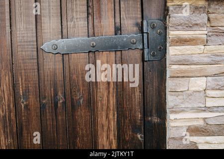 Planked varnished wooden door texture. With heavy bar hinges. With artificial stone brick cover on the wall on the side of it. Stock Photo