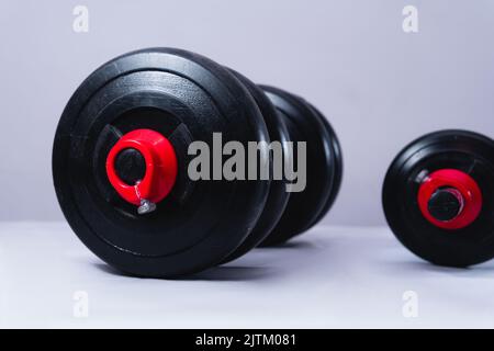 Black dumbbells on a white background. Gym weights on a table. Large dumbbell and small dumbbell for training in the gym. High quality photography. Stock Photo