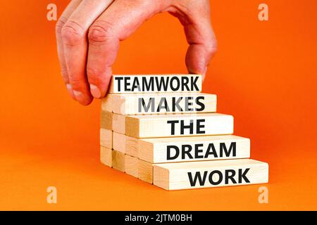 Teamwork makes dream work symbol. Concept words Teamwork makes the dream work on wooden blocks on beautiful orange background. Businessman hand. Busin Stock Photo