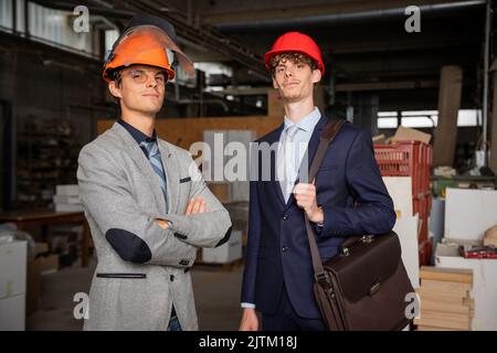 Portrait of two engineers in the factory, successful people elegantly dressed wearing protective helmets Stock Photo