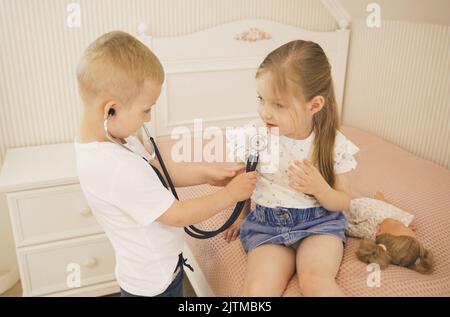 A boy listens to a girl with a stethoscope. They play doctor. Children's games. Stock Photo