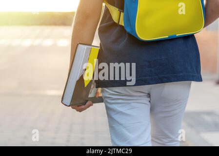 Close up of a boy on the street with a backpack in the colors of the Ukrainian flag yellow and blue and a book in his hand. Back to school Stock Photo
