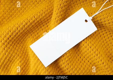 White blank rectangular clothing tag, label mockup template on yellow knitted fabric background . Price tag label with copy space for text Stock Photo