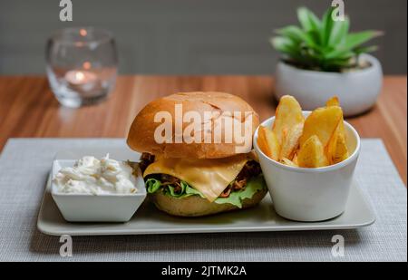 Cheesy Pulled Pork Burger with Chips and Cabbage salad, Hotel background Stock Photo