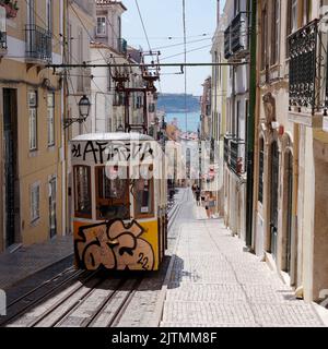 Graffiti covered Tram aka Streetcar aka Trolley in the Baixa-Chiado area of Lisbon with the River Tagus in the distance. Portugal. Stock Photo