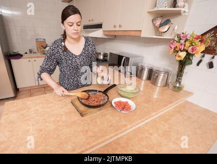 Beautiful Hispanic woman cooking while using tablet computer in kitchen ...