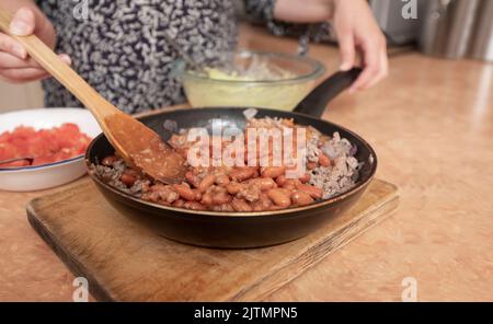 Close up of woman's hands mixing beans with ground beef using a wooden spoon in a black metal pan Stock Photo