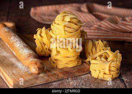 Food photography of  raw pasta, tagliatelle, fettuccine, macro, rolling pin, board Stock Photo