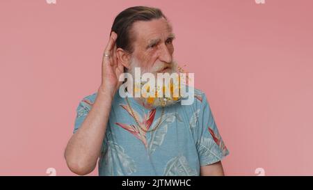 I cant hear you. What. Man trying hear you, looking confused and frowning, keeping arm near ear for louder voice, asking to repeat, to hear information, deafness. Senior grandfather on pink background Stock Photo