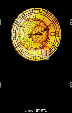 Glowing vintage yellow clock hanging on a dark wall. Stock Photo