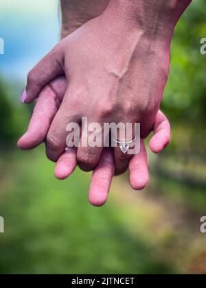 Closeup of young couple holding hands and displaying engagement ring after proposal. Stock Photo
