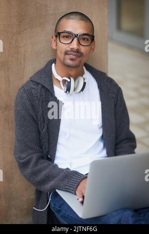 The life of a student. Portrait of a college student using his laptop while sitting outside at campus. Stock Photo
