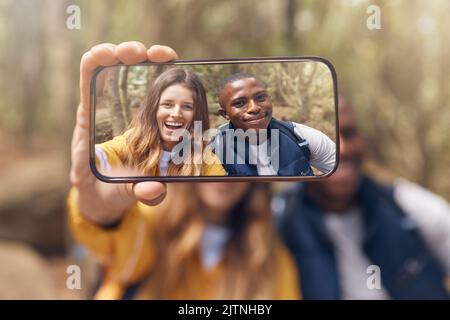 Happy couple taking a selfie on a phone while in nature on a romantic date in the forest. Multiracial, love and traveling man and woman taking picture Stock Photo