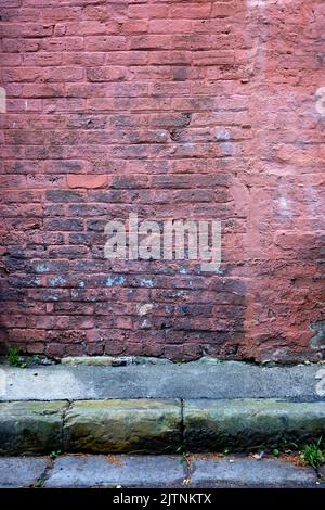 An old brick wall with faded paint with road and rain water gutter in front. Stock Photo
