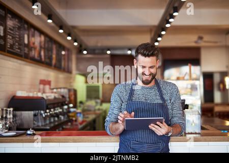 Every modern business needs technology to grow. a business owner using a digital tablet in his cafe. Stock Photo