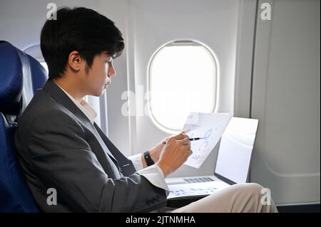 Professional Asian businessman concentrating reading and analyzing a financial data report during on the flight to his business trip. Stock Photo