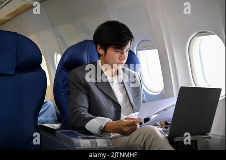 Professional and successful young Asian businessman working, managing his business tasks, preparing a meeting documents during the flight for his busi Stock Photo