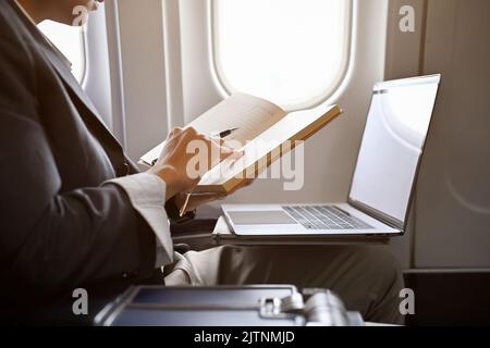 Professional young Asian businessman is on the flight, reading, checking or writing something on his notebook. cropped and close-up image Stock Photo