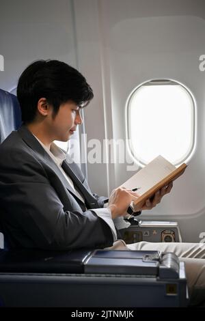 Portrait, A professional young Asian businessman is on the flight, reading, checking or writing something on his notebook. Stock Photo