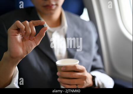 A male passenger holding a cup of water and an airsick motion sickness pills. Airsick or jet lack concept. close-up image Stock Photo