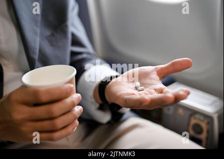 close-up image, A male passenger holding a cup of water and an airsick motion sickness pills. Airsick or jet lack concept Stock Photo