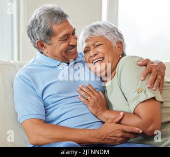 Love, care and happy senior couple hugging each other while bonding and relaxing on sofa at home. Elderly man and woman sitting on a couch in the Stock Photo
