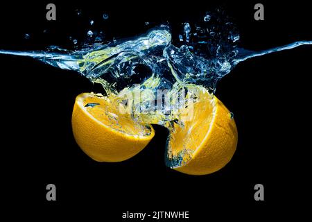 Halved lemon dropped in water with splashes isolated on black background. Stock Photo