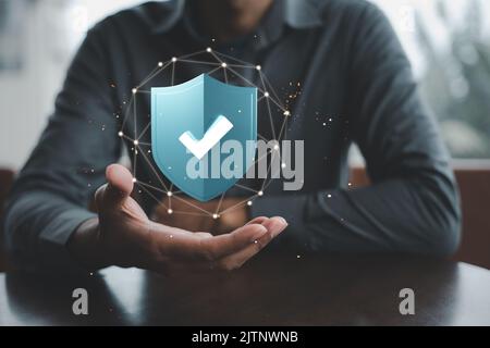 Businessman holding 3D digital shield protection with tick check mark on hand, Man sitting on desk hold network security data blue virus shield protec Stock Photo