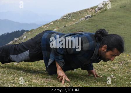 A handsome long haired Indian young man doing push-ups with three fingers in the top of mountain Stock Photo