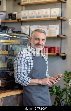 Joyous cafe employee in the apron posing for the camera Stock Photo