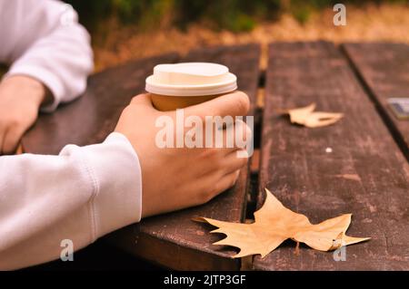 Paper glass of coffee in hand on the orange autumn leaves background  Stock Photo