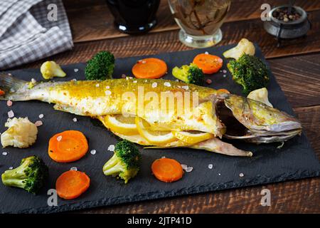 Baked sea bass fish with vegetables and greens on stone plate Stock Photo