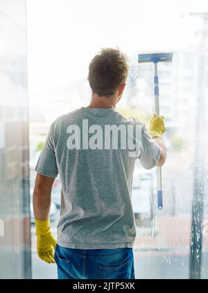 Making sure your view is unimpaired. Rearview shot of a young man cleaning the windows in the office. Stock Photo