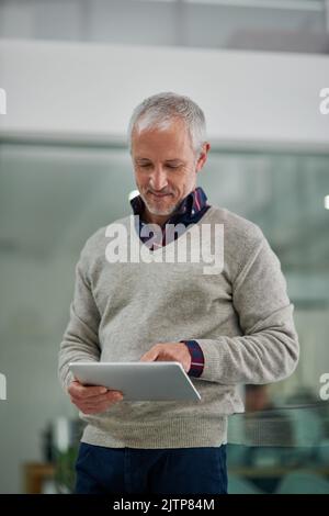 Hes a hands on businessman. a mature businessman using a digital tablet while standing in an office. Stock Photo