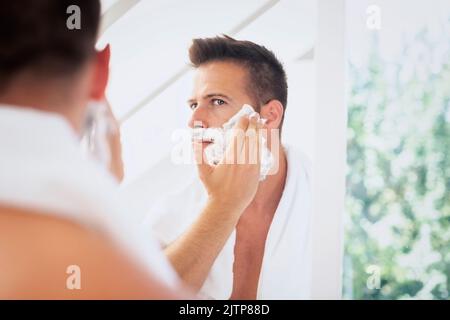 Cropped shot of a man with towel around his neck shaving his beard in the bathroom at home. Stock Photo