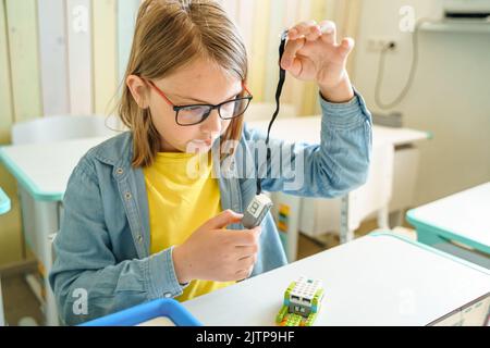 Programming work, learning robotics in elementary school. Children students assembly, launch, coding of robot. Constructor parts by instructions in ta Stock Photo
