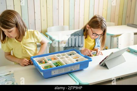 Programming work, learning robotics in elementary school. Children students assembly, launch, coding of robot. Constructor parts by instructions in ta Stock Photo