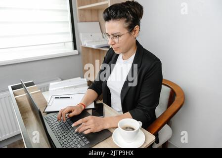 A young woman in the office working on her laptop. Real office Stock Photo