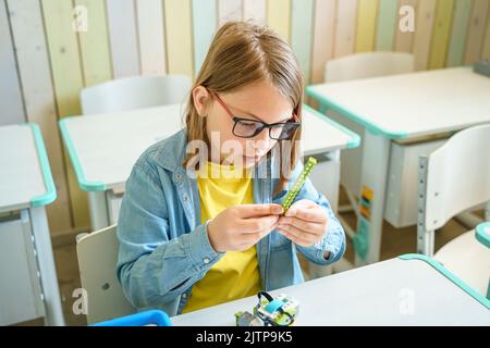 Programming work, learning robotics in elementary school. Children students assembly, launch, coding of robot. Constructor parts by instructions in ta Stock Photo