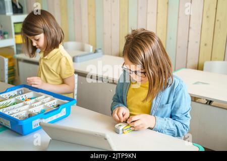 Programming work, learning robotics in elementary school. Children students assembly, launch, coding of robot. Constructor parts by instructions in ta Stock Photo