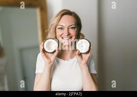 A beautiful girl holds halves of a coconut in her hands and smiles. Stock Photo