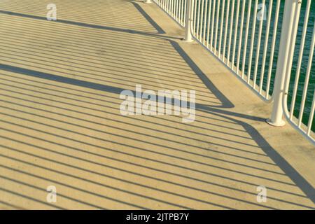 Long evening shadows from the railing on the pier. Stock Photo