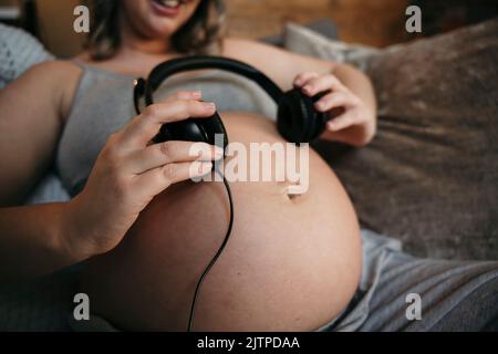 Close up of pregnant mom sitting on her sofa smiling listening to music . Stock Photo