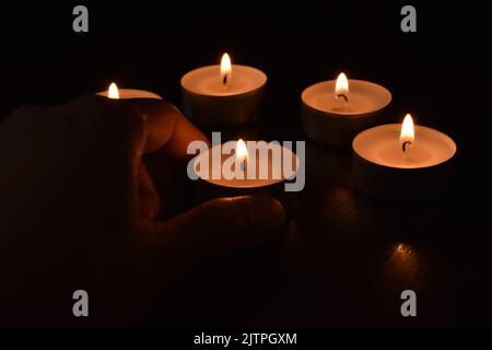 Tea light candles in the dark background.  Hand putting a candle on the table. Stock Photo